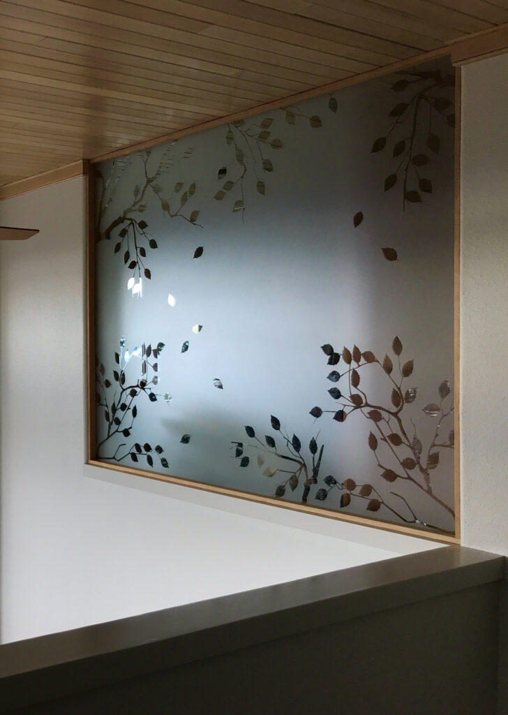 Etched glass interior window with delicate leaf branch design provides privacy while allowing soft natural light between spaces