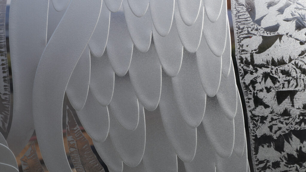 Textured close-up of carved frosted glass scales and layered detailing in a decorative interior glass partition