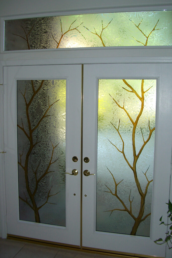 carved glass double doors with transom featuring tree branch design on frosted glass with warm backlighting