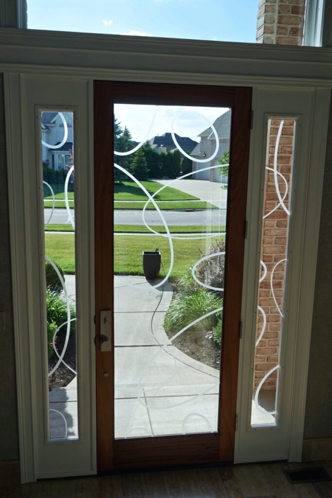 Interior view of wood front door with frosted glass oval pattern and narrow sidelights, allowing natural light while maintaining privacy.