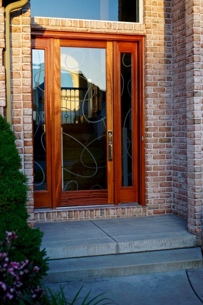 Exterior view of frosted glass front door with overlapping oval etched design, warm wood frame, and matching sidelights set in a brick exterior entryway