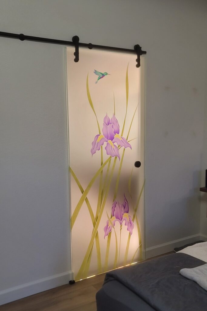 Illuminated frosted glass barn door with hand-painted purple iris flowers and hummingbird design in a modern bedroom entrance