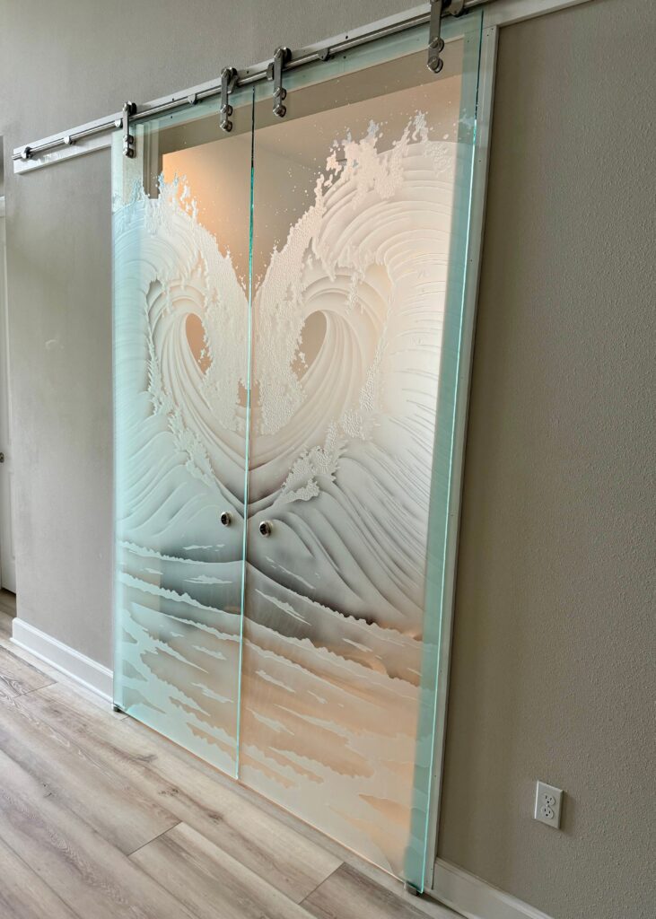 Pair of carved frosted glass barn doors with flowing wave design, mounted on stainless steel sliding hardware in a modern hallway