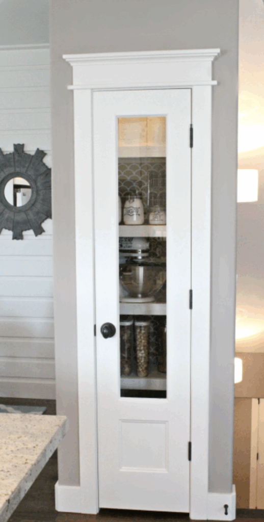 White slim single pantry door with tall narrow glass panel revealing organized pantry shelves in a modern kitchen.