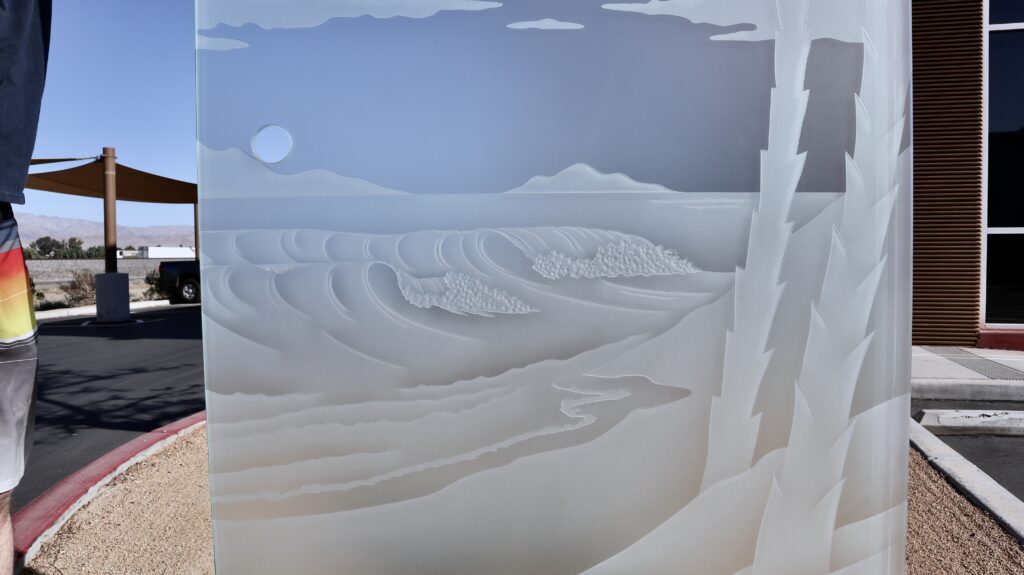 Close-up of 3D carved frosted glass showing detailed ocean waves and shoreline texture