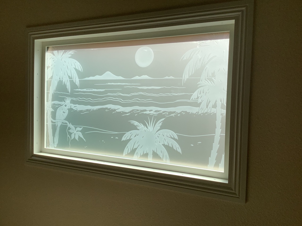 Etched glass window with tropical beach scene, palm trees, ocean waves, and cockatoo provides privacy while allowing soft natural light
