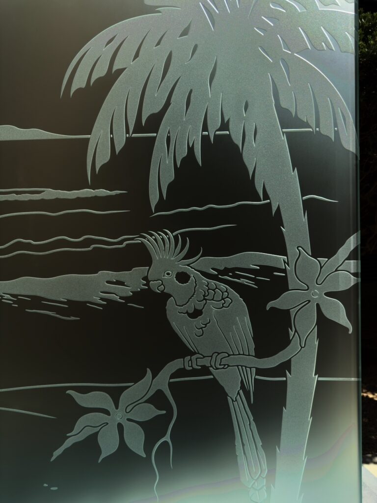 Close-up of etched glass design featuring cockatoo on palm tree with ocean background, showcasing detailed frosted glass texture
