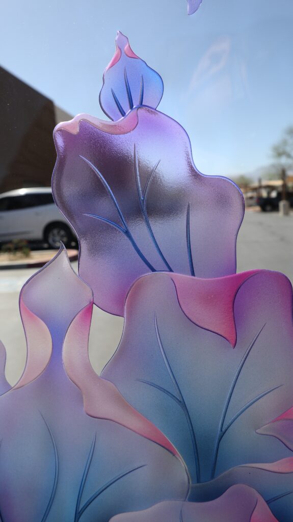 Detailed view of layered painted glass petals with carved linework on low-iron glass displaying bright translucent color and soft shading.