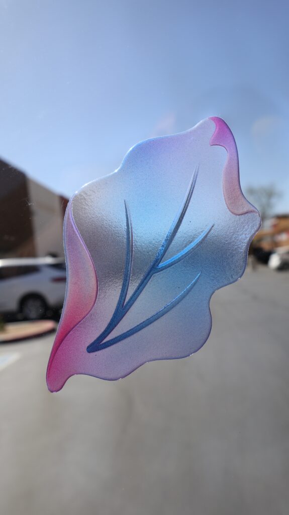 Close-up of a translucent painted glass petal design on ultra-clear low-iron glass showing soft gradients and detailed carved lines.