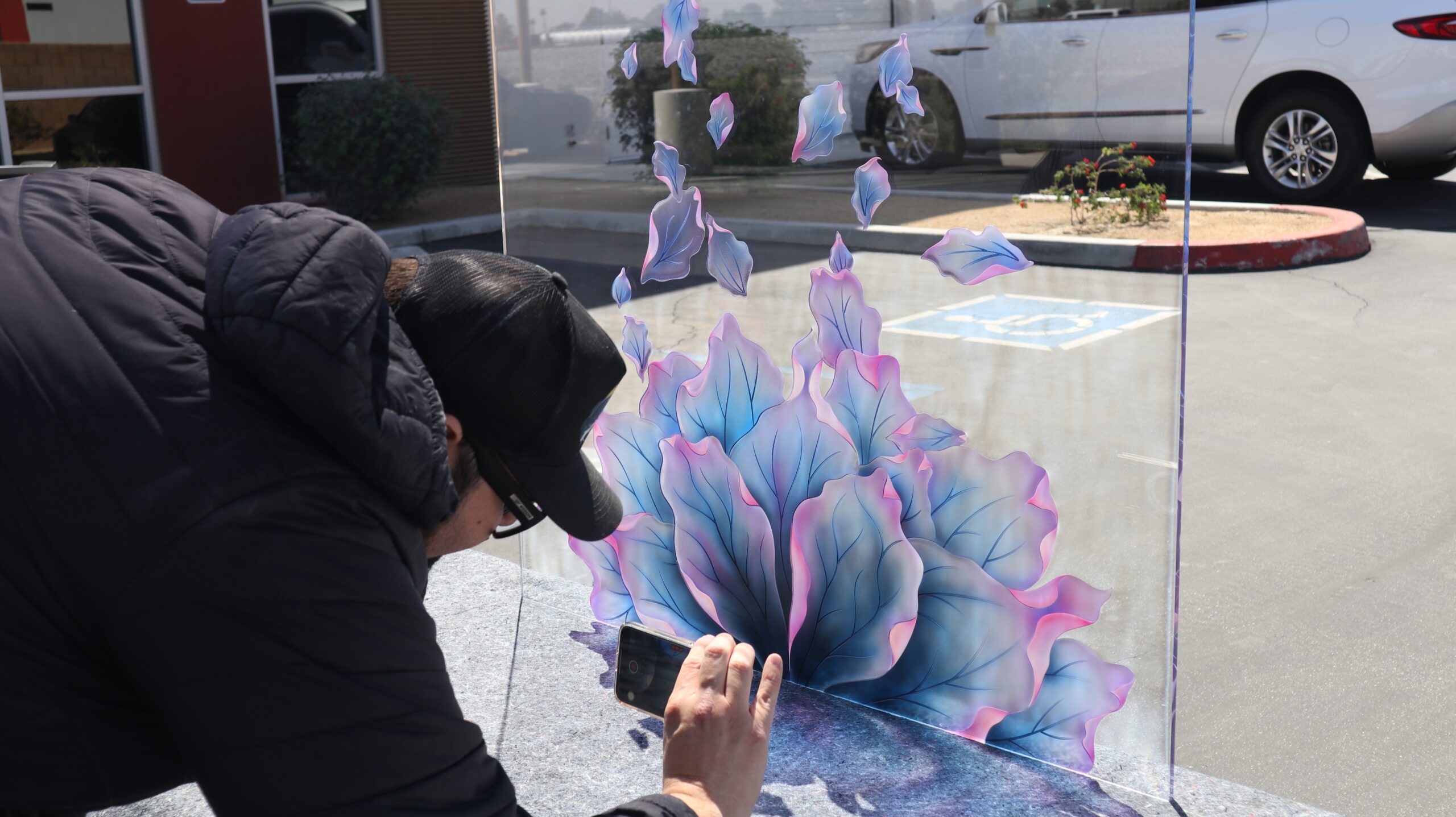 Artist photographing a painted frosted glass panel with blue and pink petal design.