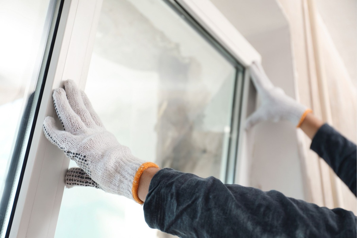Person wearing gloves installing a new white-framed window.