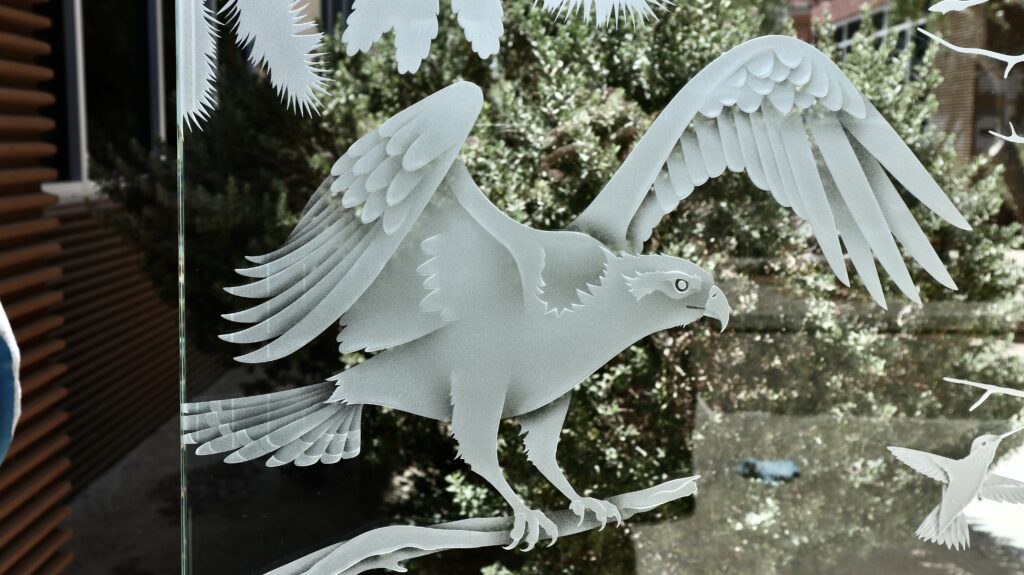 Eagle in flight carved into a Woodland Scene glass partition panel with forest-themed artwork