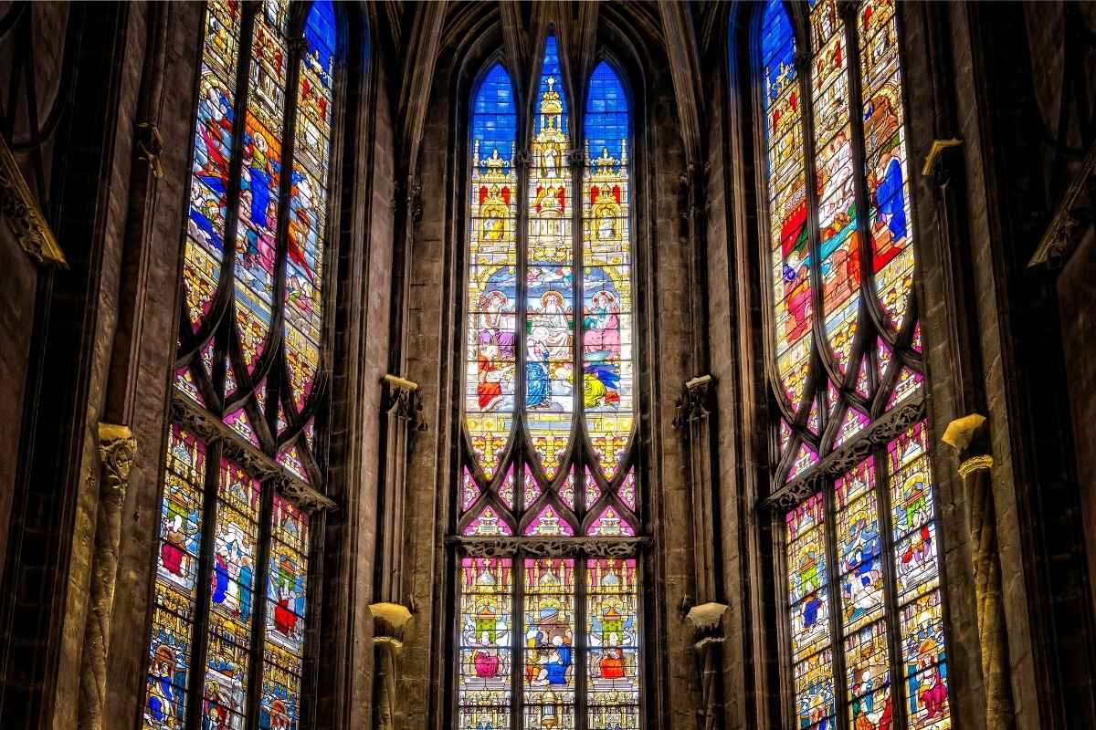 Stained glass windows in a Gothic cathedral, depicting religious scenes in vibrant colors, showcasing the historic use of stained glass as storytelling through light.