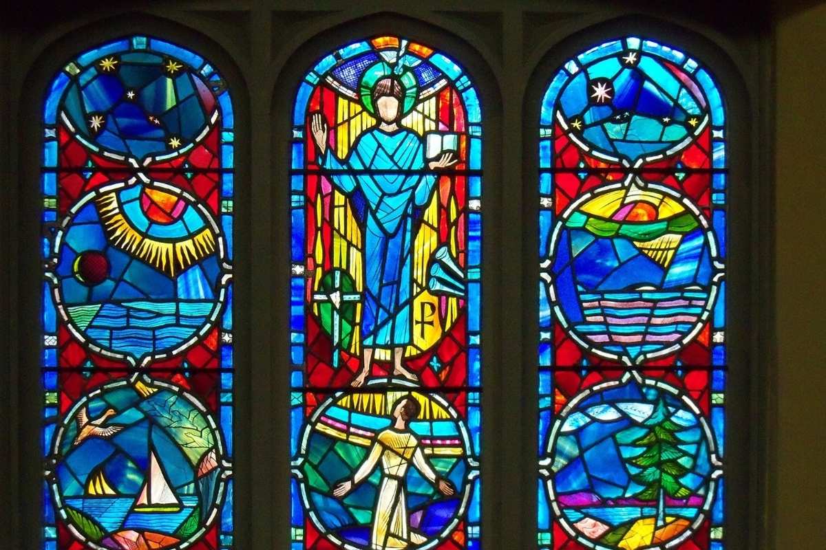 Colorful stained glass window with religious and symbolic imagery, featuring vibrant blue, red, and yellow tones commonly seen in mid-century church art.