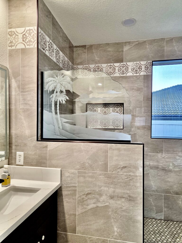 Decorative glass shower partition featuring etched palm tree and sunset landscape design.
