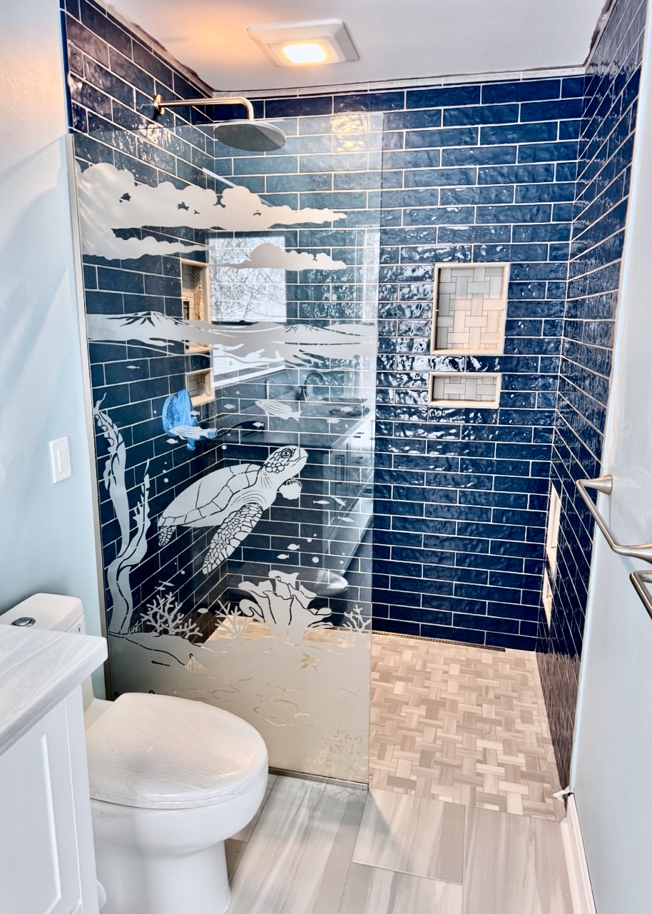 Decorative frosted glass shower panel with etched sea turtle and ocean waves design in a blue tile walk-in shower