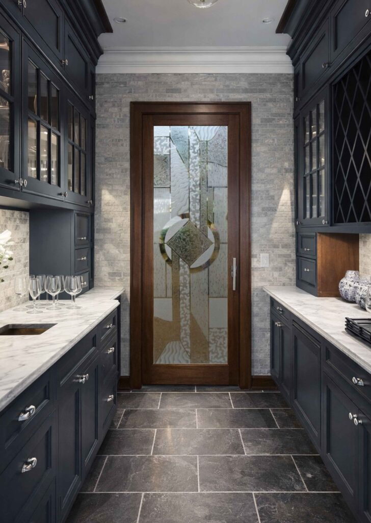 Modern transitional butler&rsquo;s pantry with navy blue cabinetry, marble countertops, and a stained wood framed frosted glass pantry door featuring Chardonnay Matrix 3D design