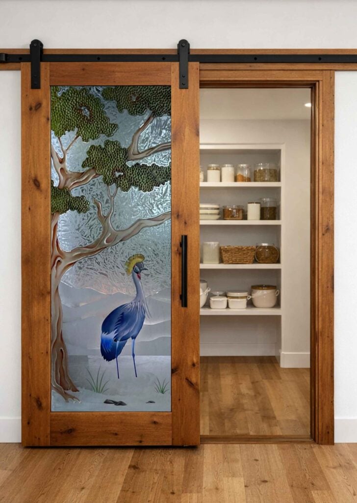 Decorative frosted glass barn door with painted crane and tree design in wood frame for kitchen pantry