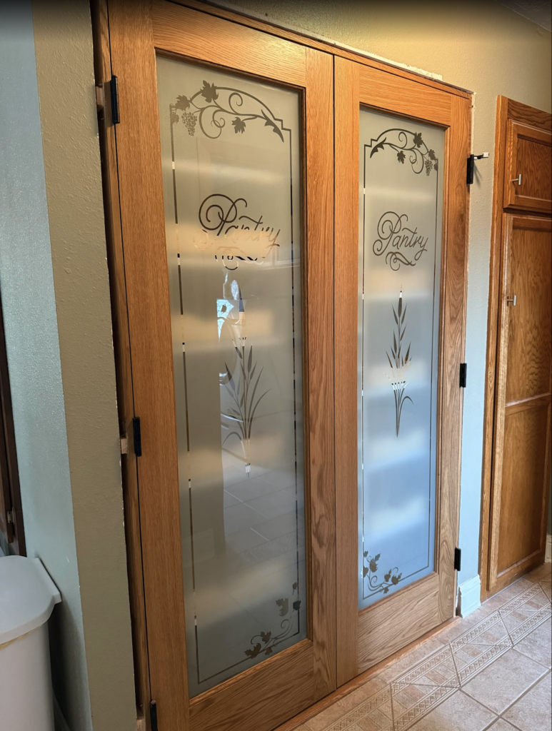Wood-framed modern pantry doors with frosted glass, decorative cattail accents, and etched “Pantry” lettering for elegant kitchen style