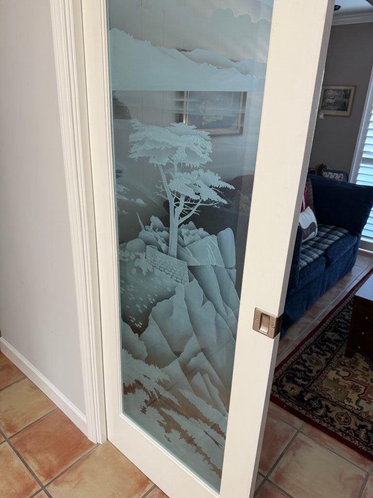Frosted glass pocket door with a Lone Cypress tree and mountain scene, creating a space-saving home office door with artistic detail.