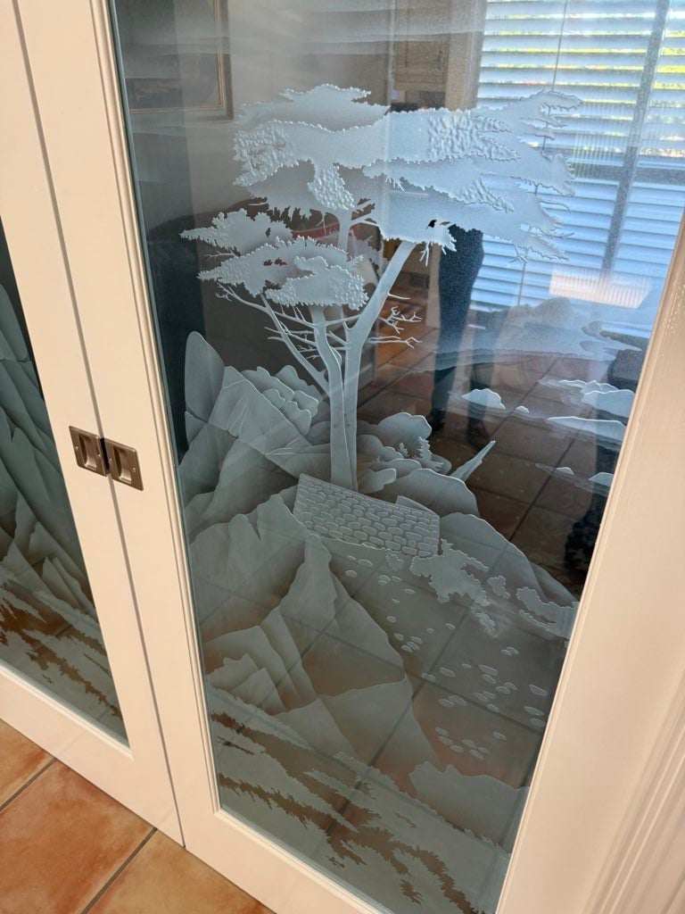 Decorative glass pocket doors with a carved Lone Cypress landscape design, adding privacy and natural light to a home office entrance.