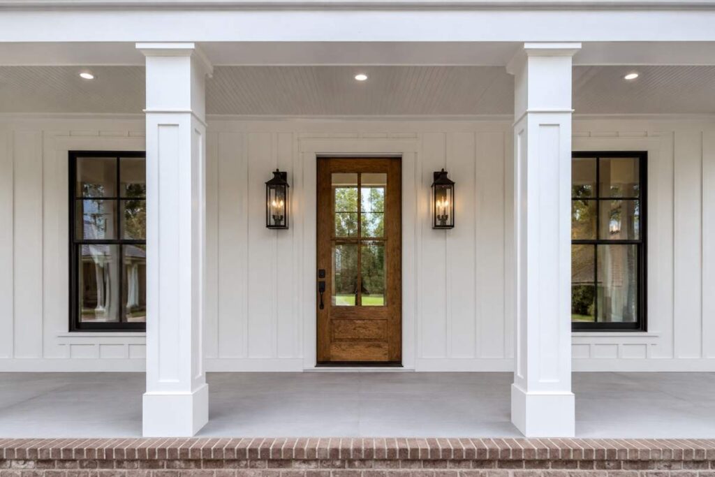 Modern farmhouse front porch with wood clear glass front door, black-framed windows, and white columns.