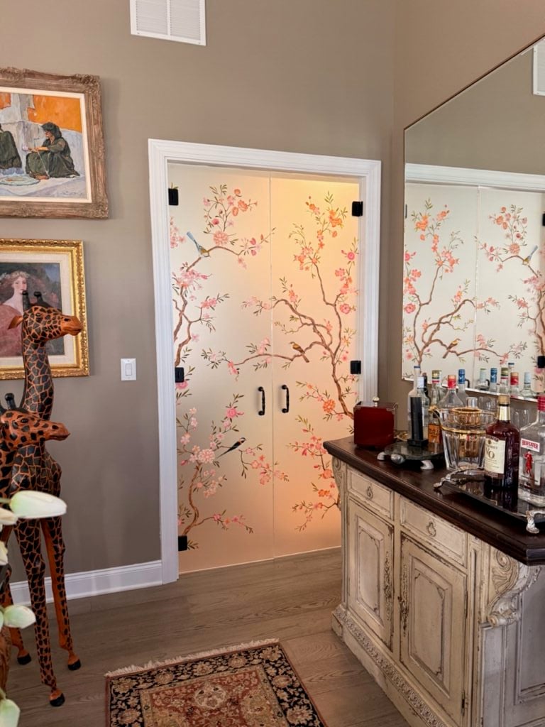 Frameless glass doors interior with painted songbird and blossom design, adding privacy, color, and natural light to a home bar entry.