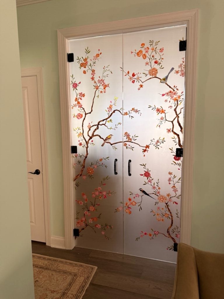 Frameless glass home office doors with a painted songbird and blossom design for a colorful, artistic entrance.