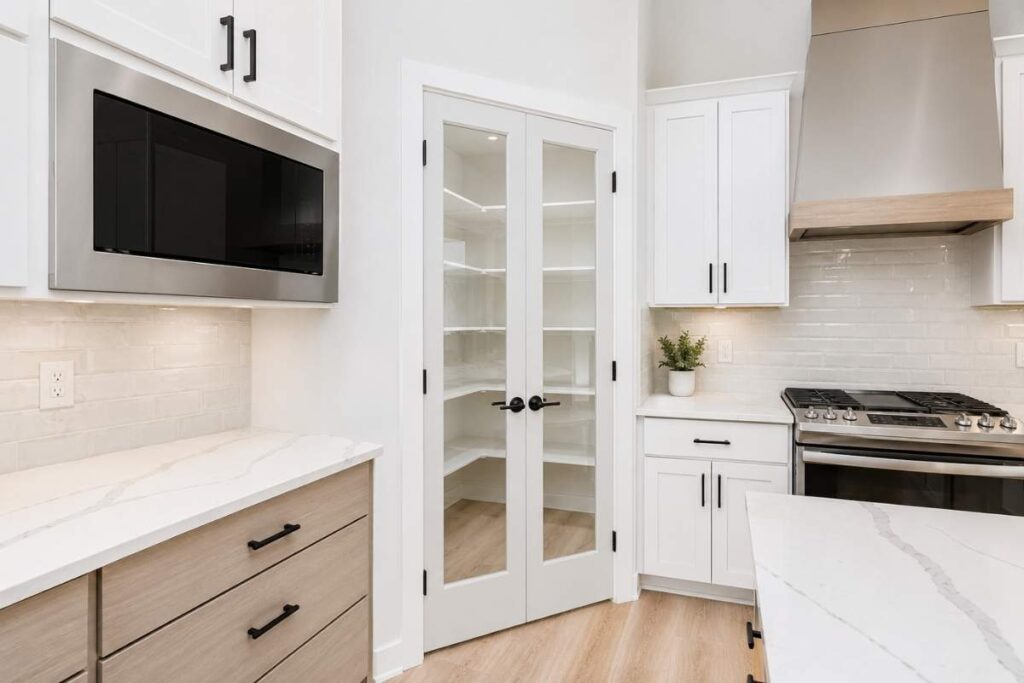 Double white wood pantry doors with clear glass panels in a modern farmhouse kitchen.