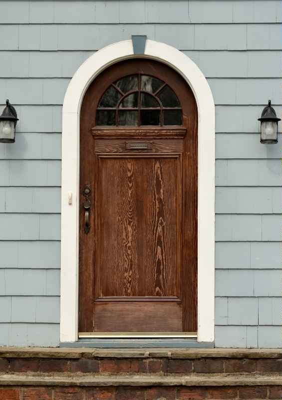 Traditional solid wood front door with an arched top and divided-light fanlight glass beneath white exterior trim.