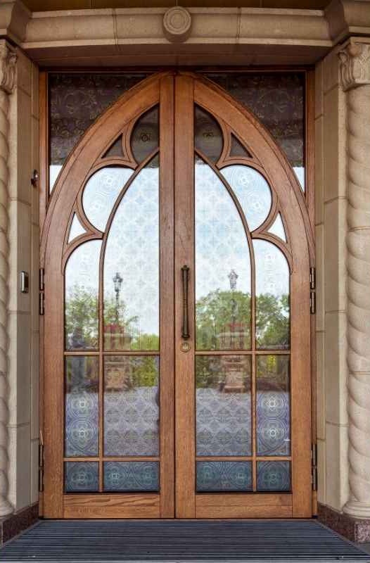 Traditional arched double wood front doors with decorative glass panels, curved muntins, and ornate architectural detailing.