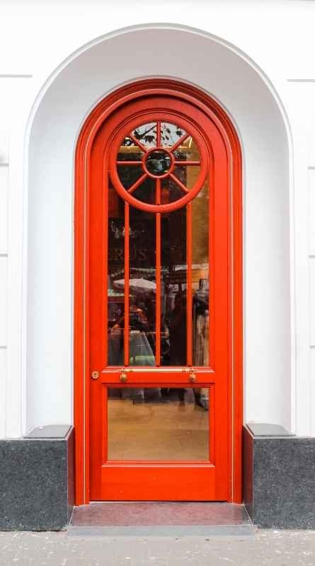 Traditional red wood front door with a tall arched glass panel, divided-light detailing, and a circular upper window.