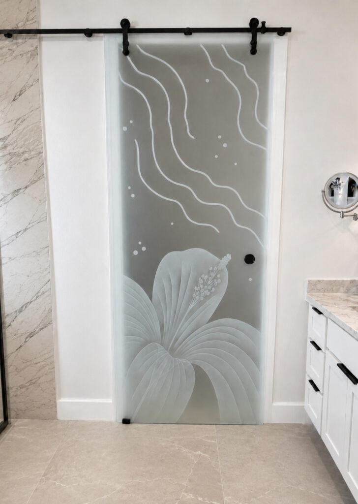 Decorative frosted glass barn door with Hibiscus Ripples carved floral design adding 100% privacy to a bright modern bathroom with marble finishes and black sliding hardware